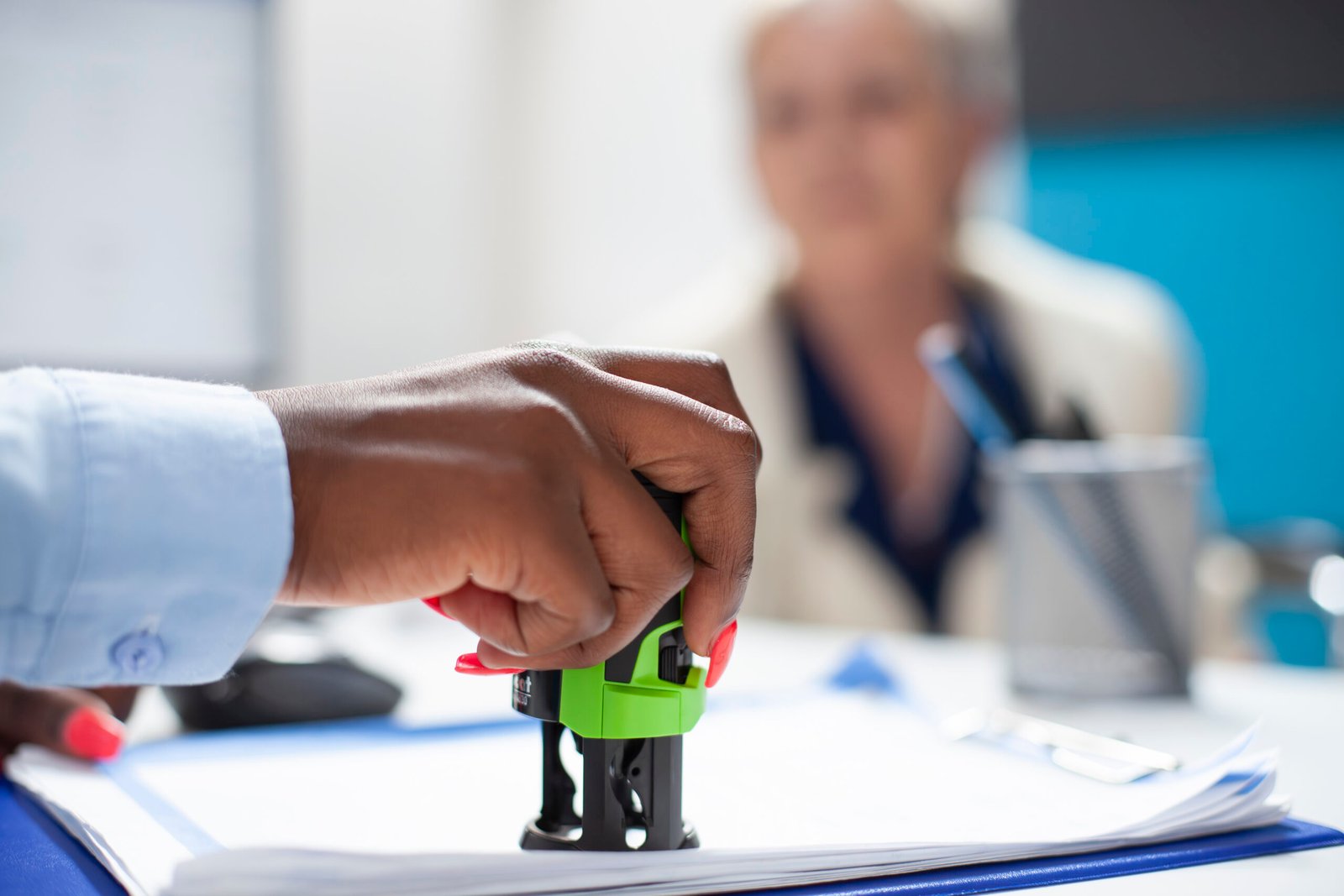 Selective focus on hand of black healthcare specialist applying stamp on document as senior woman watches attentively. Elderly patient waits as african american doctor completes her medical documents.